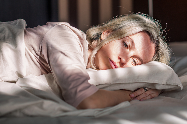Egy középkorú nő aggódó arckifejezéssel fekszik a párnán, mert álmatlanságban szenved. 