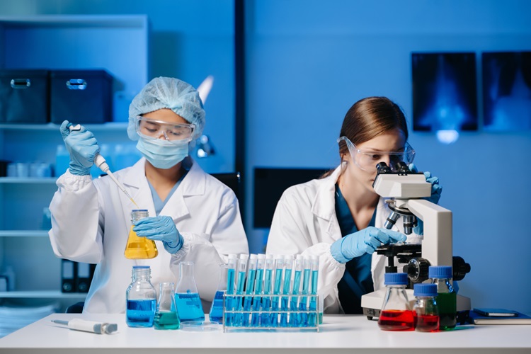 Mladí vědci provádějí výzkumná šetření v laboratoři, výzkumník v popředí používá mikroskop v laboratoři pro výrobu THCO