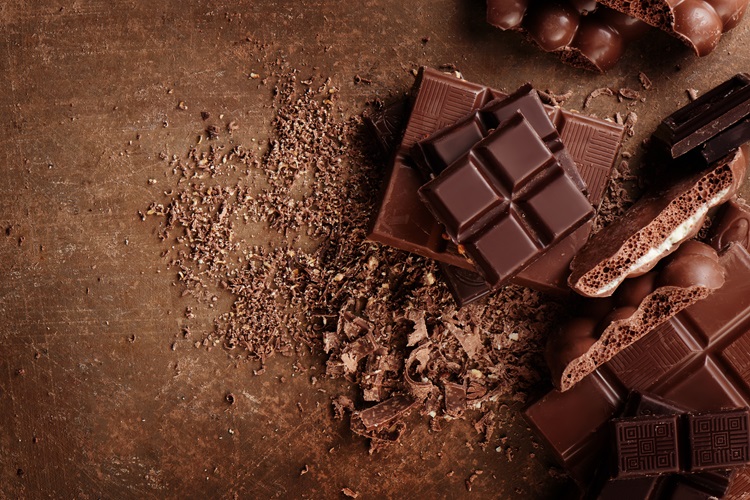 Diferentes tipos de chocolate partido con virutas y trozos de chocolate sobre fondo marrón